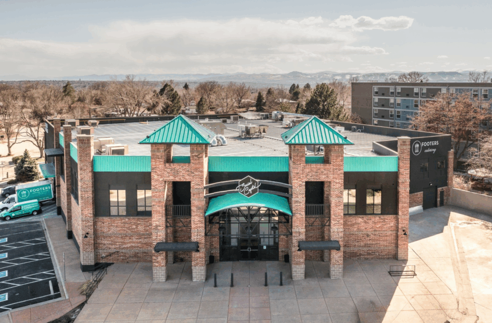 A brick building with teal roof accents and a sign reading "Footers," seen from the front on a sunny day.