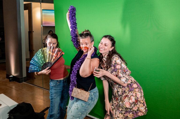 Three women pose infront of a green screen in a photobooth at a company event